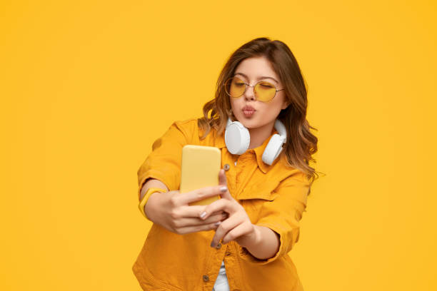 mujer enérgica con auriculares en el cuello gruñido tomando selfie en el teléfono inteligente - vibrant color yellow recreational equipment red fotografías e imágenes de stock