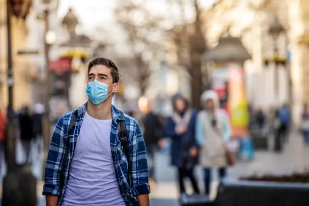 COVID-19 Pandemic Coronavirus Man in city street wearing face mask protective for spreading of Coronavirus Disease 2019. Portrait of man with face mask against SARS-CoV-2.