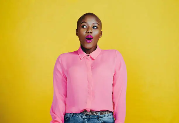 Cropped shot of an attractive young woman looking curious and surprised in studio against a yellow background