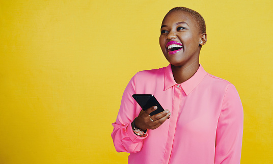 Cropped shot of an attractive young woman using her cellphone in studio against a yellow background