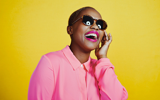 Cropped shot of an attractive young woman wearing sunglasses posing in studio against a yellow background