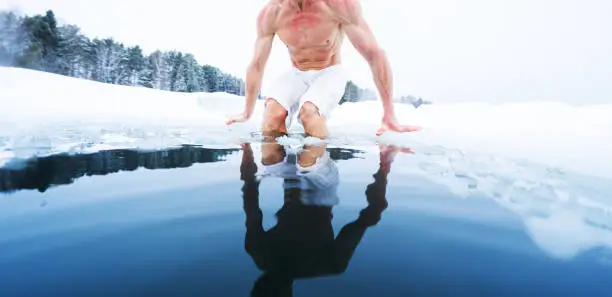 Photo of Young athletic man going to have ice bath in the winter pond