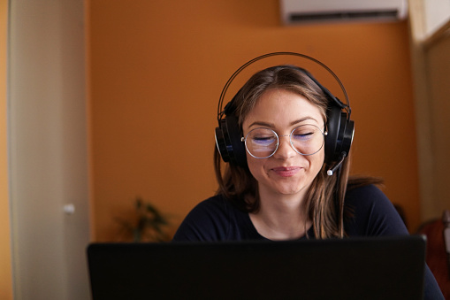 Smiling young woman wear wireless headset using laptop for e learning course online teaching on internet. Happy female teacher tutor communicating by video conference call. Work from home concept.