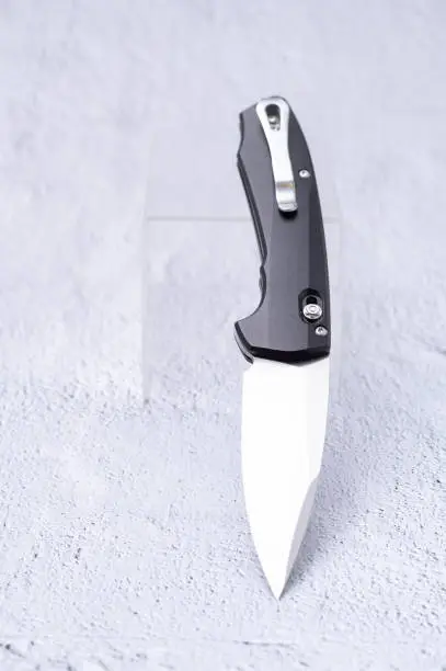 Photo of Folding knife with a clip and a black matte aluminum handle. Knife at an angle on a stand.