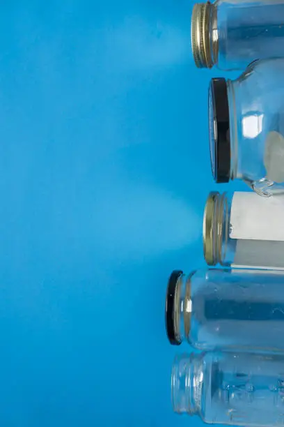 Isolated glass jars laid flat on blue background with blank empty room space room for text, copy, or copyspace on left. Recycling program or campaign image with an assortment of top view containers.