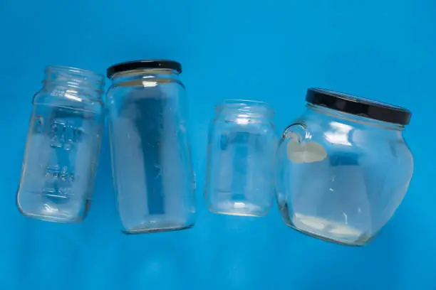 Isolated glass jars laid flat and center on blue background. Recycling program or campaign image with an assortment of top view containers. Conceptual awareness for reusable recyclables.