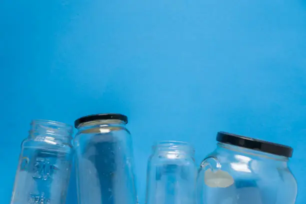 Isolated glass jars laid flat on blue background with blank empty room space room for text, copy, or copyspace on top. Recycling program or campaign image with an assortment of top view containers.