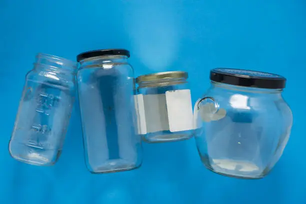 Isolated glass jars laid flat and center on blue background. Recycling program or campaign image with an assortment of top view containers. Conceptual awareness for reusable recyclables.