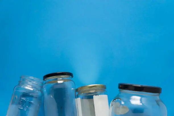 Isolated glass jars laid flat on blue background with blank empty room space room for text, copy, or copyspace on top. Recycling program or campaign image with an assortment of top view containers.