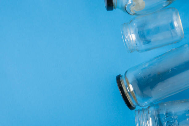 istock Isolated glass jars laid flat on blue background with blank empty room space room for text, copy, or copyspace on left. Recycling program or campaign image with an assortment of top view containers. 1223256051