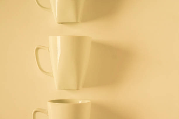 One singled out monochromatic yellow coffee mug lined up in a row on yellow background with blank empty room space for text, copy, or copy space. Modern top view concept with solid background backdrop