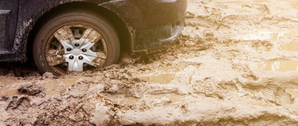 the car got stuck on a dirt road in the mud. wheel of a car stuck in the mud on the road. car on a dirt road. - mud dirt road road dirt imagens e fotografias de stock