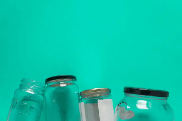 Isolated glass jars, flat on teal mint green background, blank empty room space room for text, copy, or copy space on top. Recycling program or campaign image with an assortment of top view containers