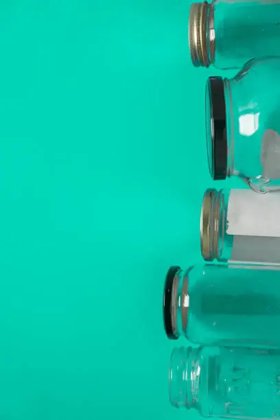 Isolated glass jars laid flat on teal mint green background, blank empty room space room for text, copy, or copy space on left. Recycling program or campaign image, assortment of top view containers.