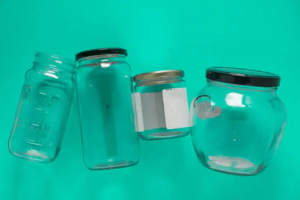 Isolated glass jars laid flat and center on teal mint green background. Recycling program or campaign image with an assortment of top view containers. Conceptual awareness for reusable recyclables.