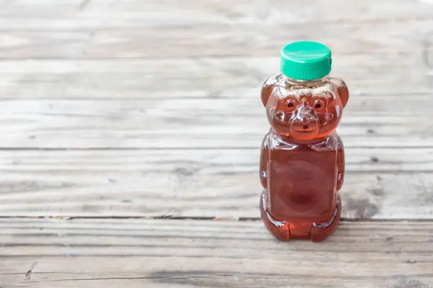 Healthy organic natural sweetener, raw honey - from bees. Golden brown liquid in bear shaped bottle with green cap. Isolated on solid wooden background with blank empty room space for text or copy.