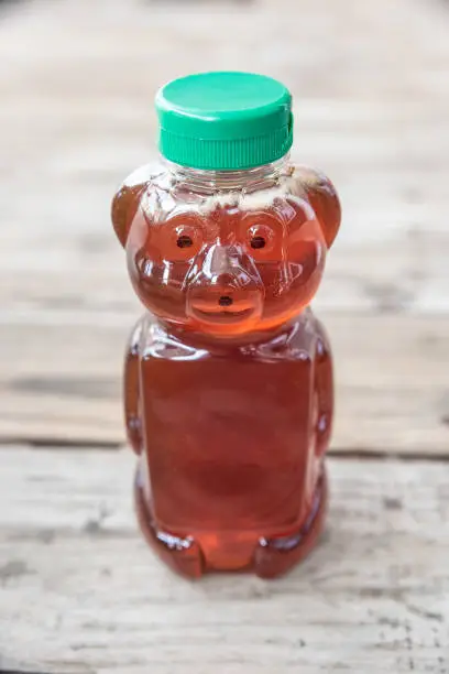 Healthy organic natural sweetener, raw honey - from bees. Golden brown liquid in bear shaped bottle with green cap. Isolated on solid wooden background with blank empty room space for text or copy.