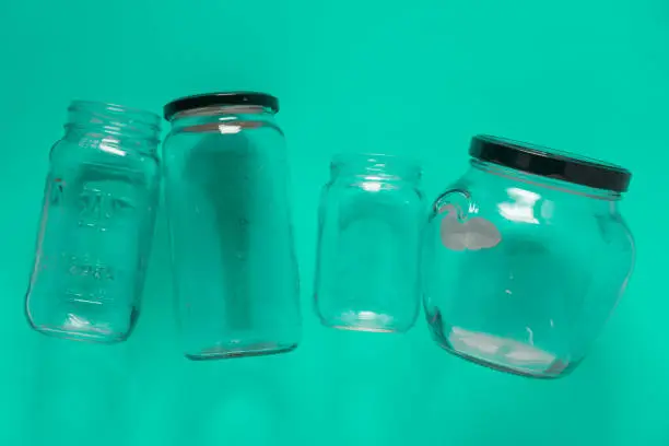 Isolated glass jars laid flat and center on teal mint green background. Recycling program or campaign image with an assortment of top view containers. Conceptual awareness for reusable recyclables.