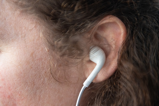 This is a close up photograph of the ear of a woman in her 30s listening to headphones while social distancing.
