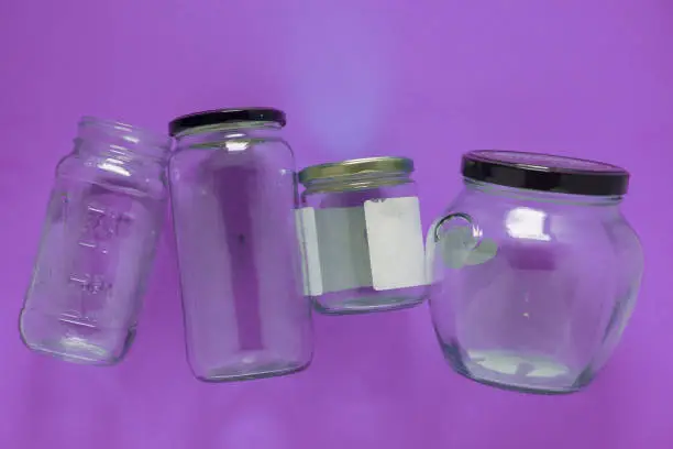 Isolated glass jars laid flat and center on violet purple background. Recycling program or campaign image with an assortment of top view containers. Conceptual awareness for reusable recyclables.
