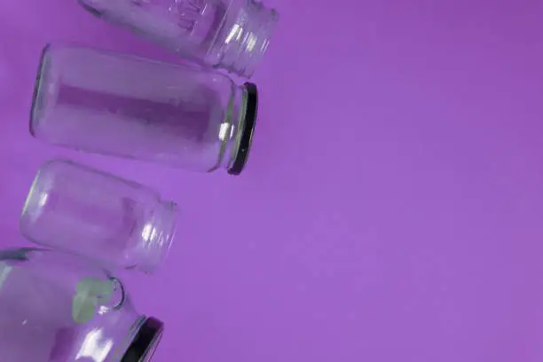 Isolated glass jars, flat on violet purple background, blank empty room space room for text or copy on right. Recycling program or campaign image with an assortment of top view containers.