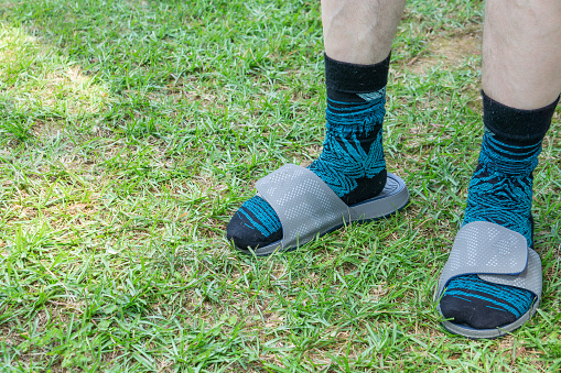 White caucasian man wearing patterned socks with gray checker designed sandals. Male fashion footwear mistake. Outside on green grass. Blank empty room space for text or copy. Unfashionable in America