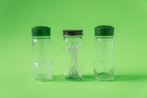 3 Glass spice jars on lime green background with blank empty room space for text or copy. Three kitchen bottles recycled and reused to store cotton swabs bathroom essentials. Recyclable junk garbage.