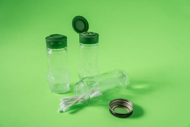 3 Glass spice jars on lime green background with blank empty room space for text or copy. Three kitchen bottles recycled and reused to store cotton swabs bathroom essentials. Recyclable junk garbage.