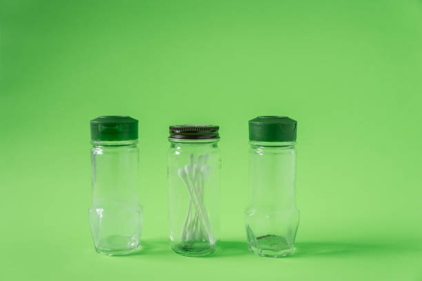 istock 3 Glass spice jars on lime green background with blank empty room space for text or copy. Three kitchen bottles recycled and reused to store cotton swabs bathroom essentials. Recyclable junk garbage. 1223260511