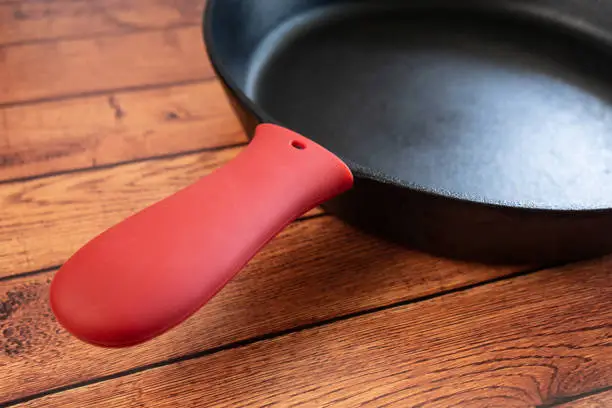 Protect from burning hands with a silicone cover for your cast iron skillet or pan. Burn protection from cooking accidents. Close up of handle with red grip for heat resistance.