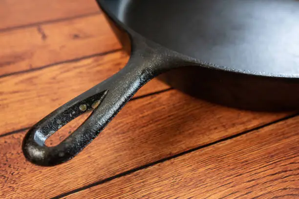 Rusted cast iron skillet handle - rusty culinary problem - downside to this traditional and heavy metal pan on wooden table. Close up of rust. Blank empty room space for text or copy.