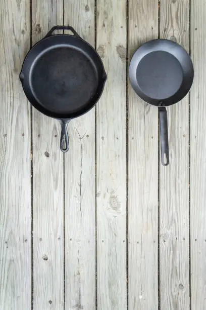 Traditional vs new cookware battle - cast iron versus carbon steel or teflon. Wooden background. Healthier cooking utensil options. Blank empty text room for copy space on bottom.
