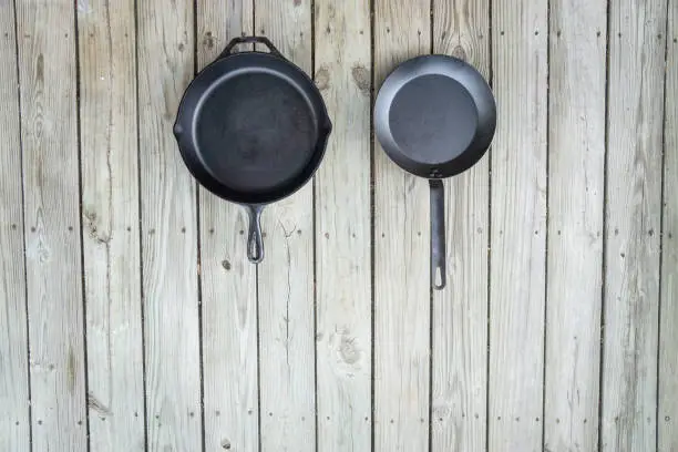 Traditional vs new cookware battle - cast iron versus carbon steel or teflon. Wooden background. Healthier cooking utensil options. Blank empty text room for copy space on bottom.