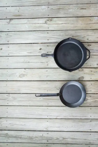 Cast iron vs carbon steel vs teflon pans. Skillet cookware battle comparison for healthier cooking options from stove to oven to campfire. Blank empty room for text or copy space on left.