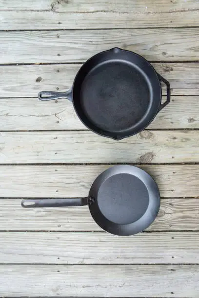 Traditional cast iron vs carbon steel versus teflon cooking options - blank empty room for text or copy space. Two cookware pieces - kitchen stove to oven to campfire. Durability test. Head to head.
