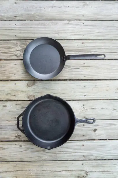 Traditional cast iron vs carbon steel versus teflon cooking options - blank empty room for text or copy space. Two cookware pieces - kitchen stove to oven to campfire. Durability test. Head to head.