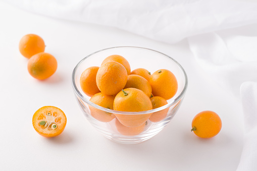tropical kumquat fruit in a glass transparent bowl on a white background next to a cloth