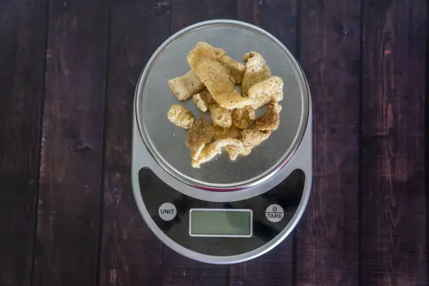 High fat low carb healthy snack - pork rinds measured on kitchen scale. Blank empty room for text or copy space. Keto friendly food for low carbohydrate diet.