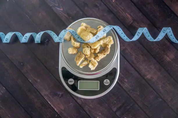 High fat low carb healthy snack - pork rinds measured on scale with measuring tape. Blank empty room for text or copy space.