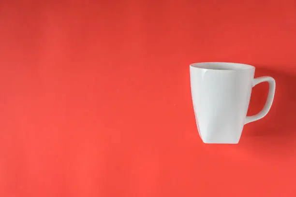 White coffee mug on red background - isolated with copy space on left.
