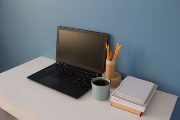 istock Empty home office of creative entrepreneur with black laptop on white table during lunch break. Modern workspace with blue cup of coffee and yellow pencils in paper tube as reusable packaging concept. 1223263752
