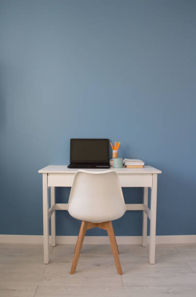 istock Vertical composition of empty workspace of creative entrepreneur with black laptop on white table. Modern home office with blue wall as background 1223263756