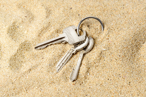 Ring with three home keys on a sea sand. Forget or fall house keys while relaxing on the beach. Accidentally drop keys. Lose bunch of apartment keys concept. Close-up.