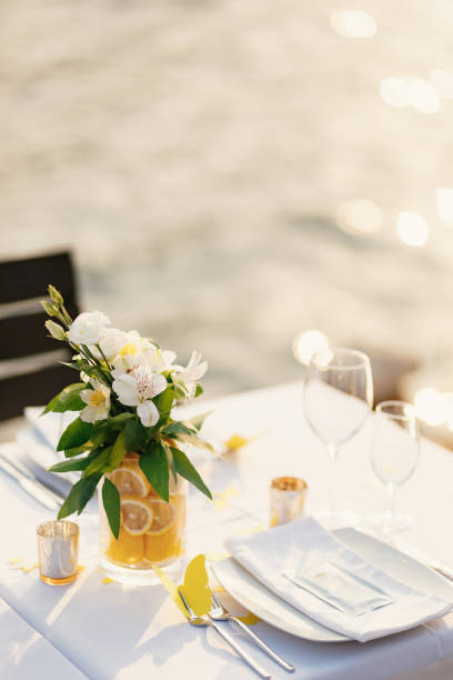 istock Wedding dinner table reception. Glass transparent bath with sliced lemons and a bouquet of white Alstromeri, on the table against the background of the glare of water in the sunset light 1223268503