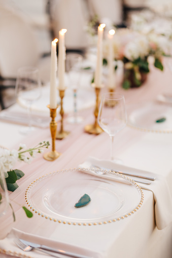 Close-up of wildcard with gold beads, transparent glass. Runner of pink silk. Candles in golden candlesticks and flowers in the center of the table.