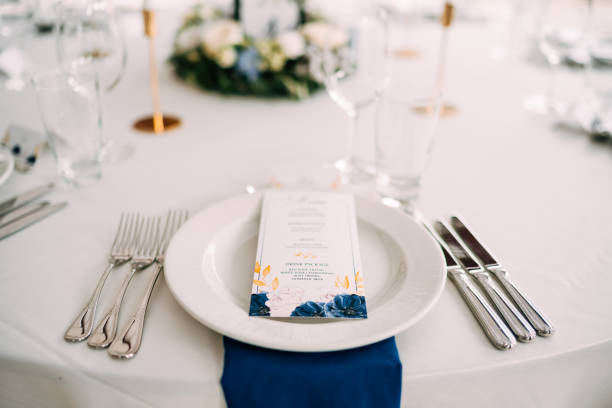 istock Wedding dinner table reception. White plate on the table, three forks on the left, three knives on the right. The wedding menu is in the plate. Top view 1223269325