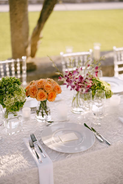 istock Wedding dinner table reception. View from above on white round plates close-up. Bouquets of pink, orange, green flowers. Pink roses, small orange roses. Top view 1223272094