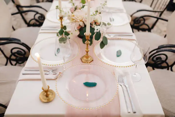 Close-up of wildcard with gold beads, transparent glass. Runner of pink silk. Candles in golden candlesticks and flowers in the center of the table.