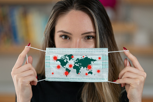 Portrait of a woman wearing a surgical mask with a virus and a map of the world. Mask protects us from corona virus all over the world