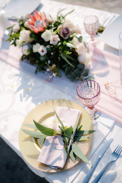 Wedding dinner table reception. Gold plate with pink cloth napkin and olive leaves. Raspberry old glass glass. A floral arrangement in the center of the table.